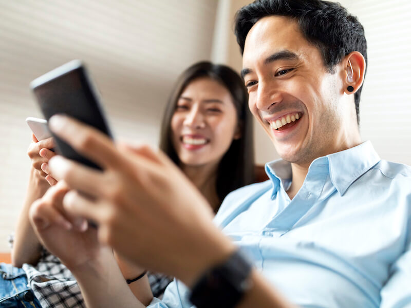 Man wearing hearing aids happily using a cell phone